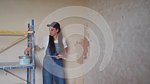 Professional plasterer female spackles the wall, applies and spreads plaster on a spatula in overalls and ball cap