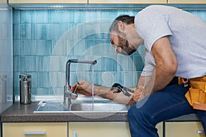 Professional plumber looking concentrated, using pipe wrench while examining and fixing faucet in the kitchen