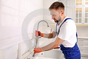 Professional plumber repairing water tap in kitchen