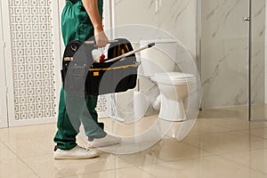 Professional plumber with toolbox near toilet bowl in bathroom, closeup