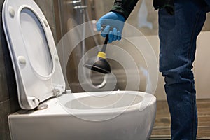 Professional plumber using plunger to unclog a toilet bowl.