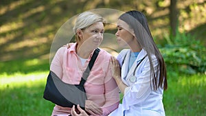 Professional podiatrist comforting injured old lady arm sling, recovery advise
