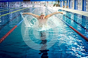 Professional polo player, male swimmer, performing the butterfly stroke technique at indoor pool, swimming practice