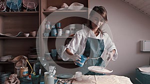 Professional potter decorating and painting a dish after she has baked it in the kiln