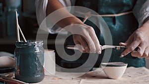 Professional potter decorating and painting a dish after she has baked it in the kiln