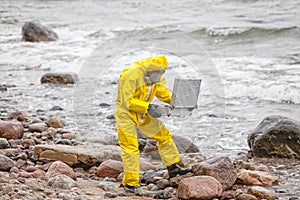 Professional in protective coveralls with mini lab on contaminated rocky sea shore photo
