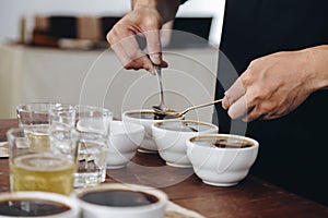 professional Q Grader preparing to test and inspecting the quality of coffee and skim off the coffee grounds from ceramic cup on