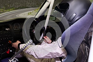 A professional racer in a black helmet and a homologated suit sits in the sports seat of a car with a roll cage for drifting and photo