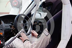 A professional racer in a black helmet and a white homologated suit sits in the sports seat of a car with a roll cage for drifting photo