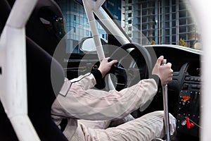 A professional racer in a black helmet and a white homologated suit sits in the sports seat of a left-hand drive car with a roll photo