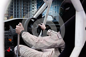 A professional racer in a black helmet and a white homologated suit sits in the sports seat of a right-hand drive car with a roll photo