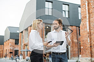 Professional real estate agent wearing white shirt holding in hand and giving keys to young buyer.