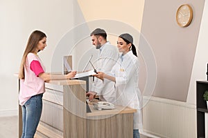 Professional receptionists working with patient at desk in clinic