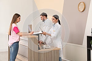 Professional receptionists working with patient at desk in clinic photo