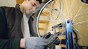 Professional repairman is fixing bicycle wheel spokes straightening them with special tools and rotating wheel to check