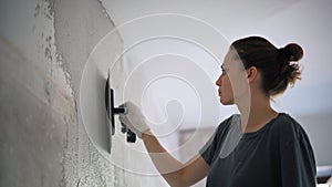 A professional repairwoman puts a plaster on the wall with a spatula.