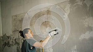 A professional repairwoman puts a plaster on the wall with a spatula.