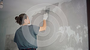A professional repairwoman puts a plaster on the wall with a spatula.