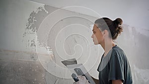 A professional repairwoman puts a plaster on the wall with a spatula.