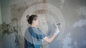 A professional repairwoman puts a plaster on the wall with a spatula.