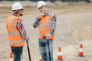 professional road construction workers in orange vests and protective helmets in the middle on the terrain