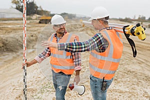 Professional road construction workers in orange vests and protective helmets in the middle on the terrain