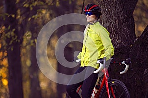 Professional Road Cycling. Cute Caucasian Female Cyclist With Road Bike Resting Outdoors Near Old Tree Against Autumn Background