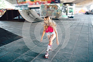 Professional rollerblader is riding in special training room. She is squatting during the trick. Her hair is waving.