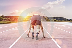 Professional runner taking ready to start position against bright sunlight