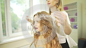 Professional salon hairdresser stylist putting jewelry hair diadem accesory pearl tiara on blonde wavy female model head