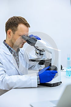 Scientist man doing chemical experiment, making analyzing, looking sample under microscope