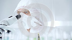 Professional scientist in protective gear is using microscope in a laboratory setting, close-up of researcher. Science