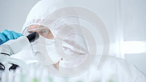 Professional scientist in protective gear is using microscope in a laboratory setting, close-up of researcher. Science