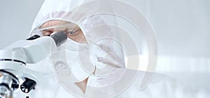 Professional scientist in protective gear is using microscope in a laboratory setting, close-up of researcher. Science