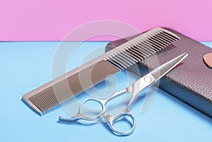 Professional scissors and a comb for a hairdresser on blue and pink background close -up.