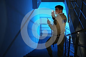 Professional security guard with flashlight and portable radio set on stairs in room