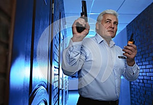 Professional security guard with gun and radio set in dark hallway