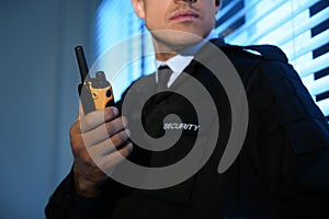 Professional security guard with portable radio set near window in dark room, closeup