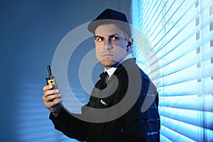 Professional security guard with portable radio set near window in room