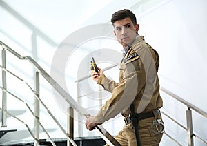 Professional security guard with radio set on stairs indoors