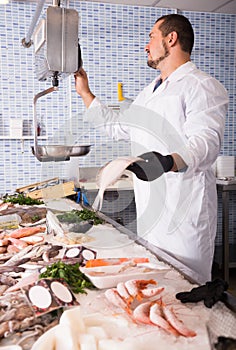 Professional seller in white cover-slut standing near fish counter