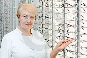 Professional senior female optician offering glasses in optics store