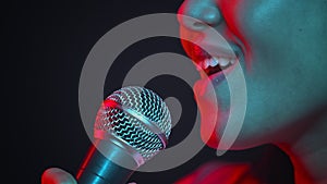 Professional singer. Young excited unrecognizable woman singing into microphone, performing in neon lights, side view