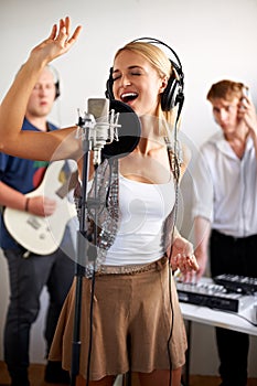 Professional, singing and happy woman with microphone, headphones and band performance with talent. Recording studio