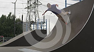 Professional skater teen engaged blond rides skateboard in skate park. Skateboarder slides down high ramp slide in