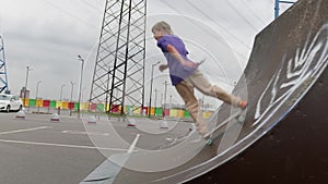 Professional skater teen engaged blond rides skateboard in skate park. Skateboarder slides down high ramp slide in