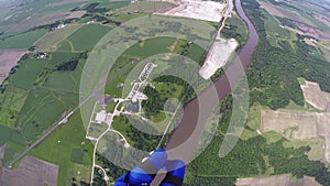 Professional skydiver parachuting in blue sky above forest and river. Landscape