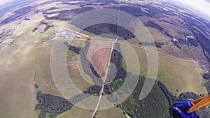 Professional skydiver parachuting over green field in sunny day. Landscape