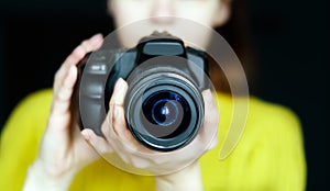 Professional Slr Camera In Women`s Hands. A young girl is holding a photo camera in her hand, looking at the lens. Look into the l