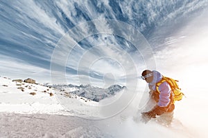 Professional snowboarder with a backpack leaving the cloud of snowy powder at sunset on a background of epic clouds and
